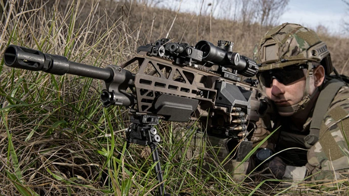 a military guy in tall grass holding an fn evolys